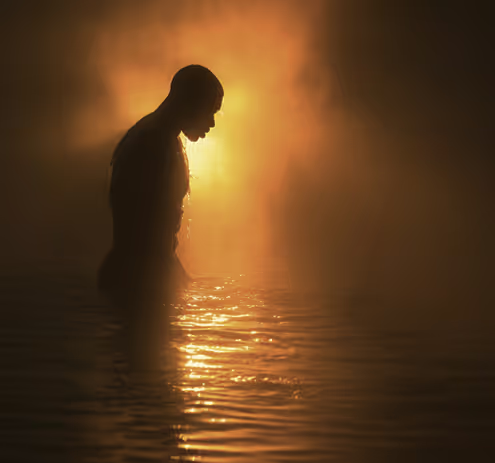 A man standing in a body of water at sunset.