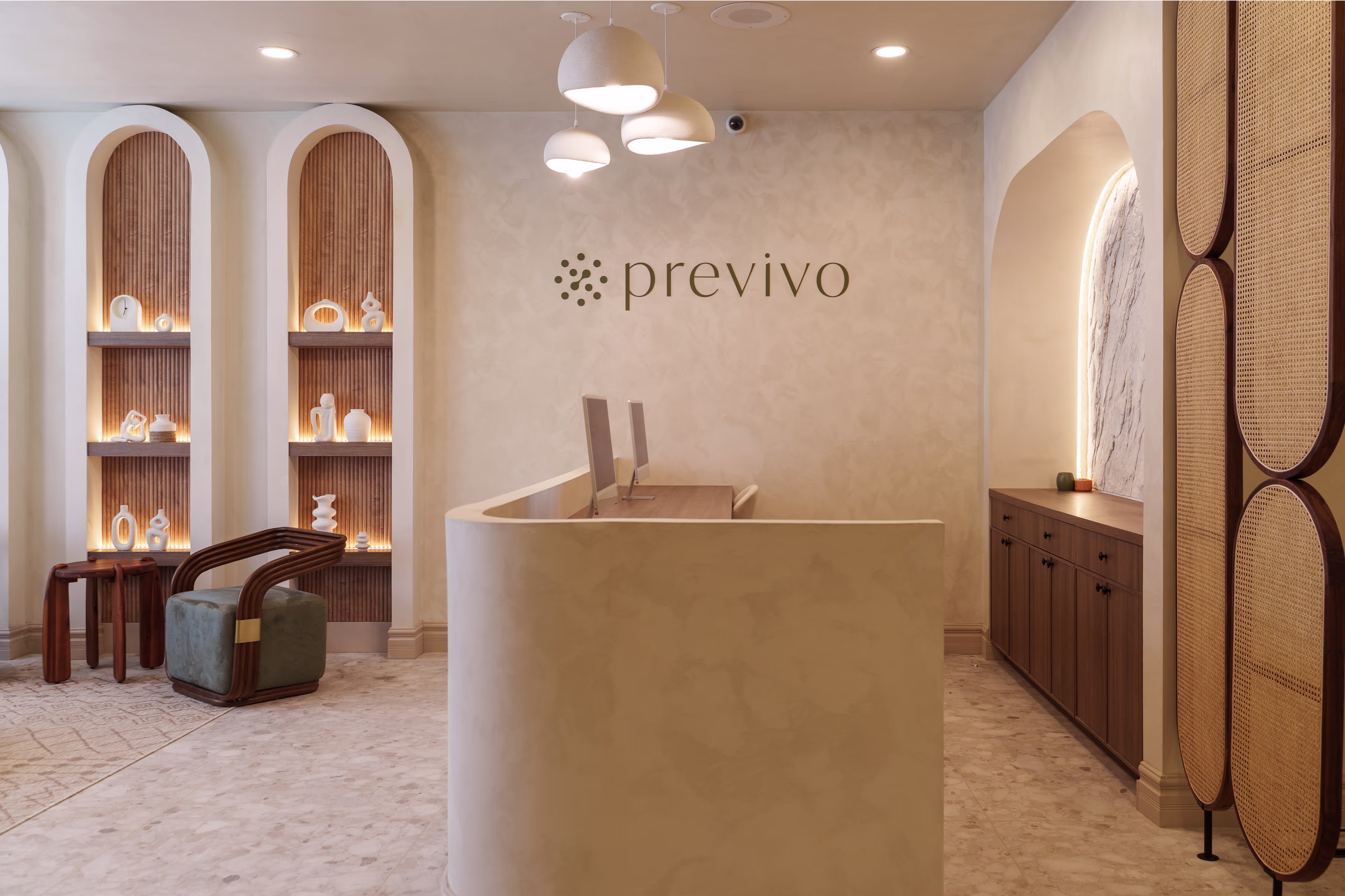 Modern reception area with curved desk, two computers, decorative shelves, and seating under pendant lights.