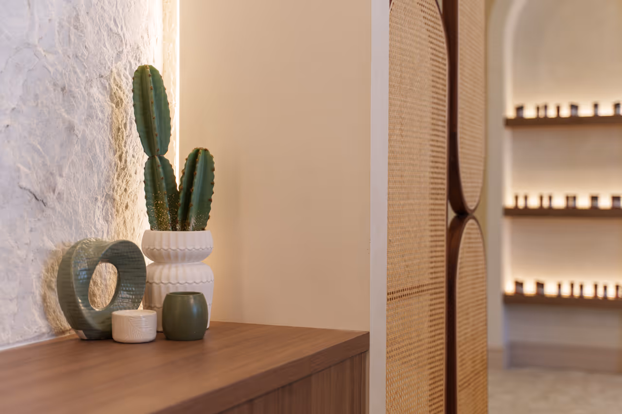 Decorative cactus in white pot with small candles and ceramic vase on wooden table by textured wall.
