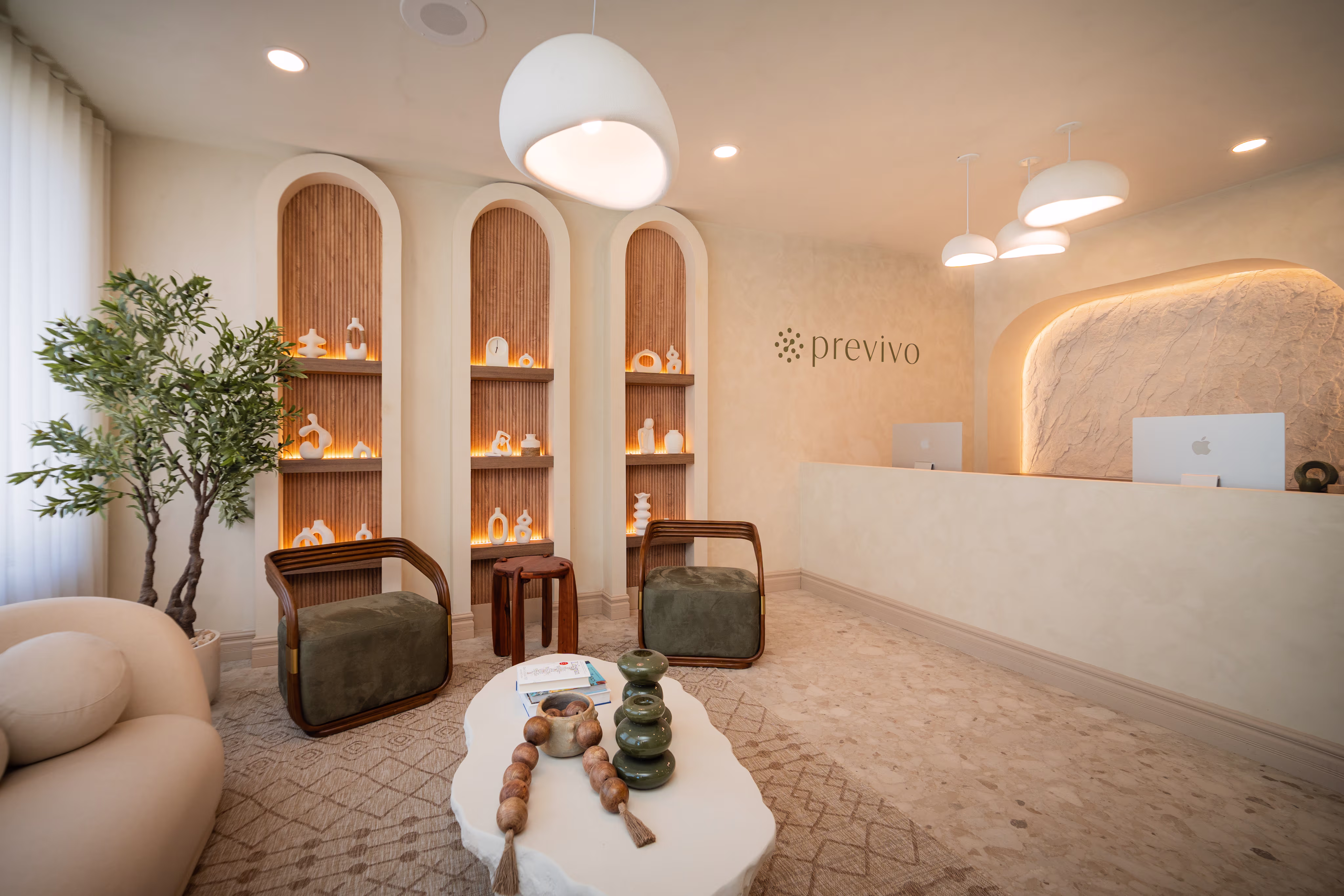 Modern waiting room with green chairs, white table, decorative shelves, and a reception desk with Previvo logo.