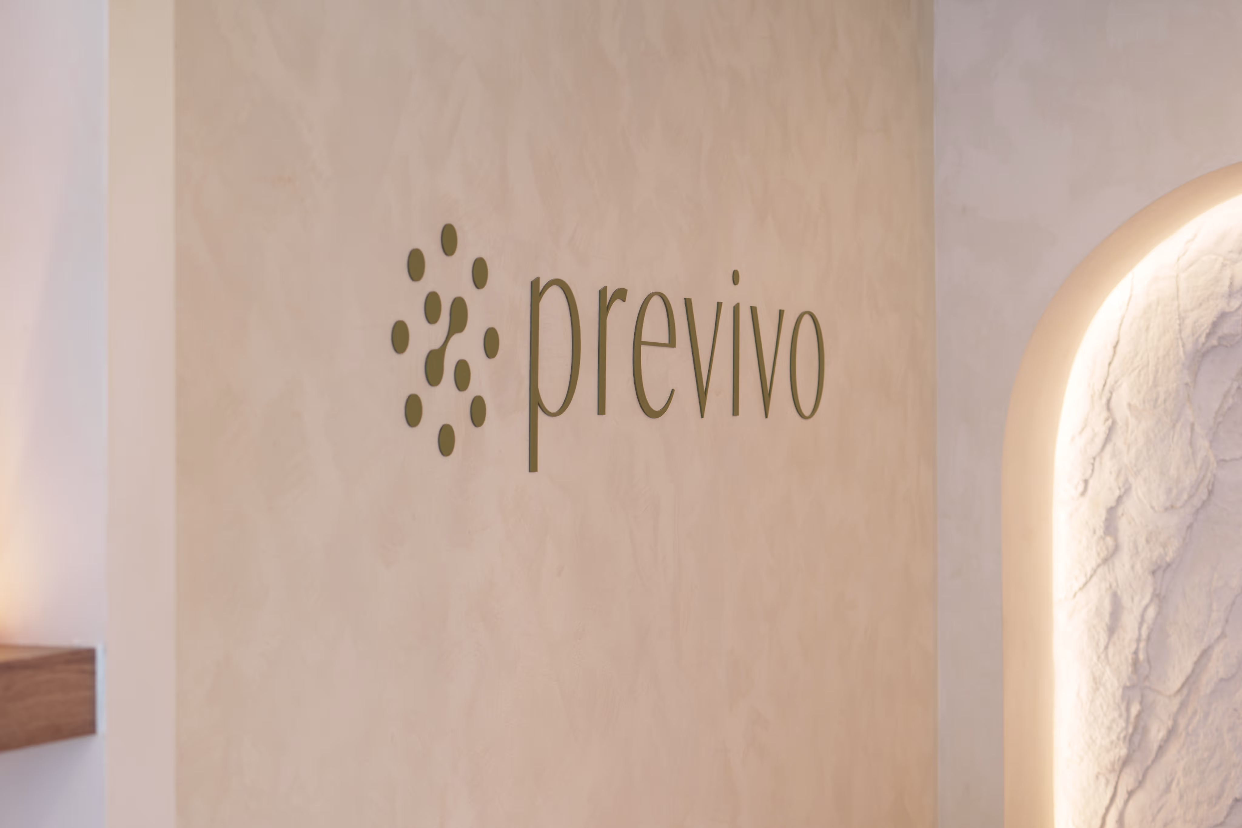 Wall with the word 'previvo' and a circular dots logo next to it in a softly lit space.