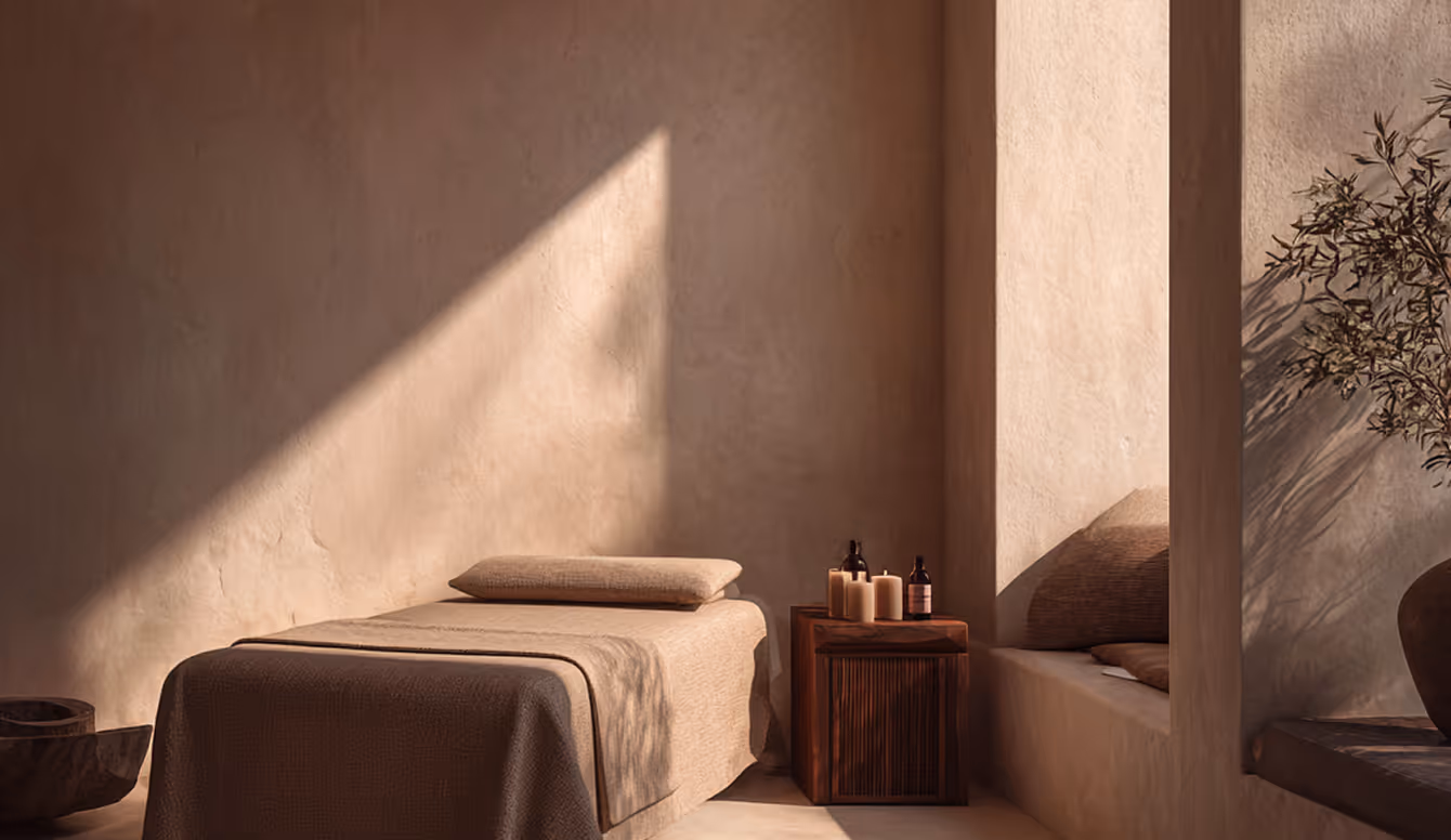 Cozy massage table with pillow beside wooden table holding candles in a warm, minimal spa room.