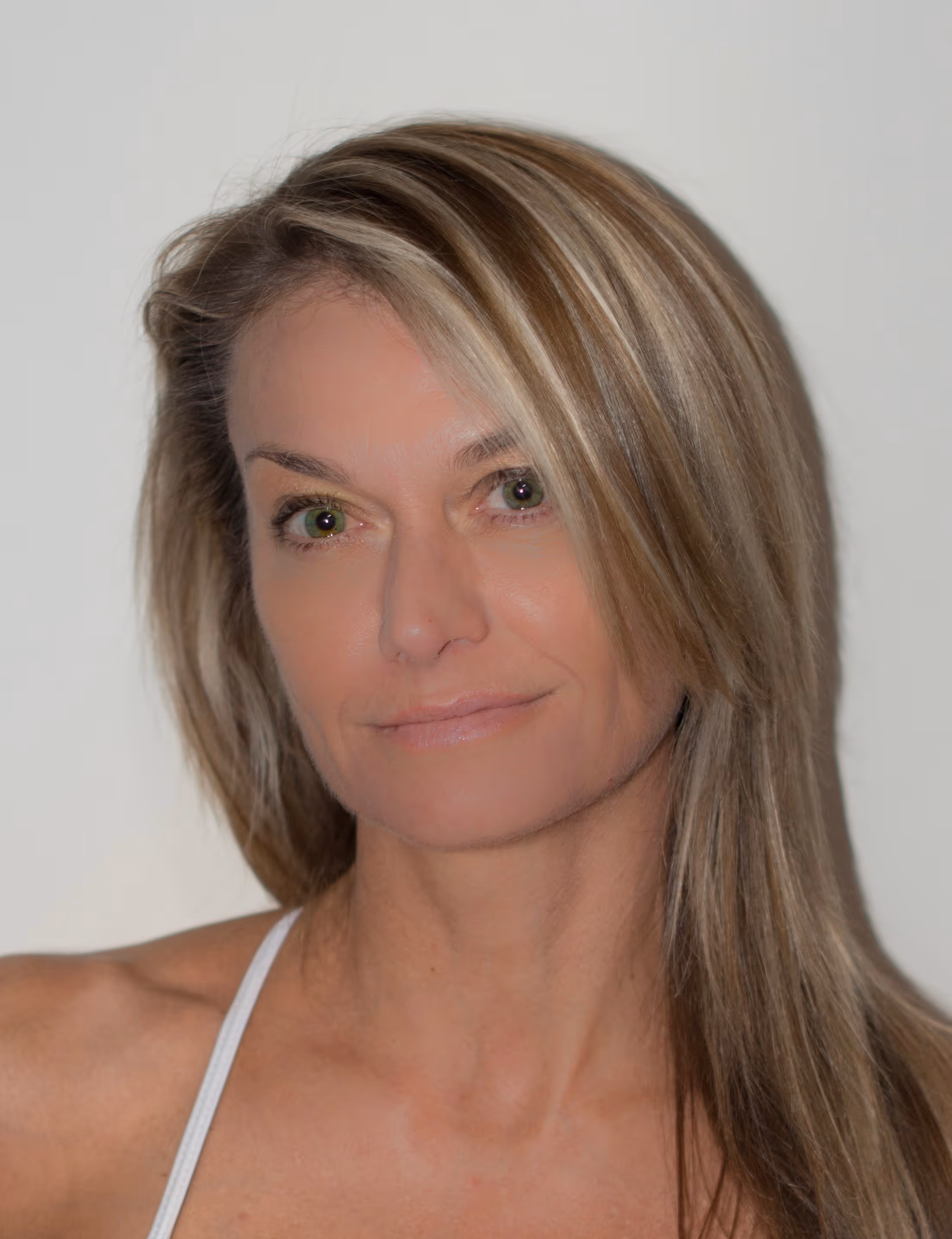 Portrait of a woman with long blonde hair and green eyes wearing a white strap top.