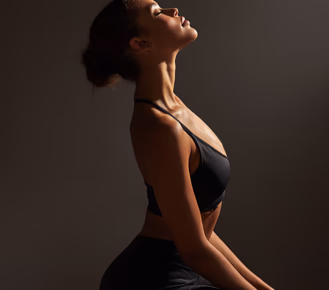 Woman in black sportswear posing with head tilted back and eyes closed against dark background.