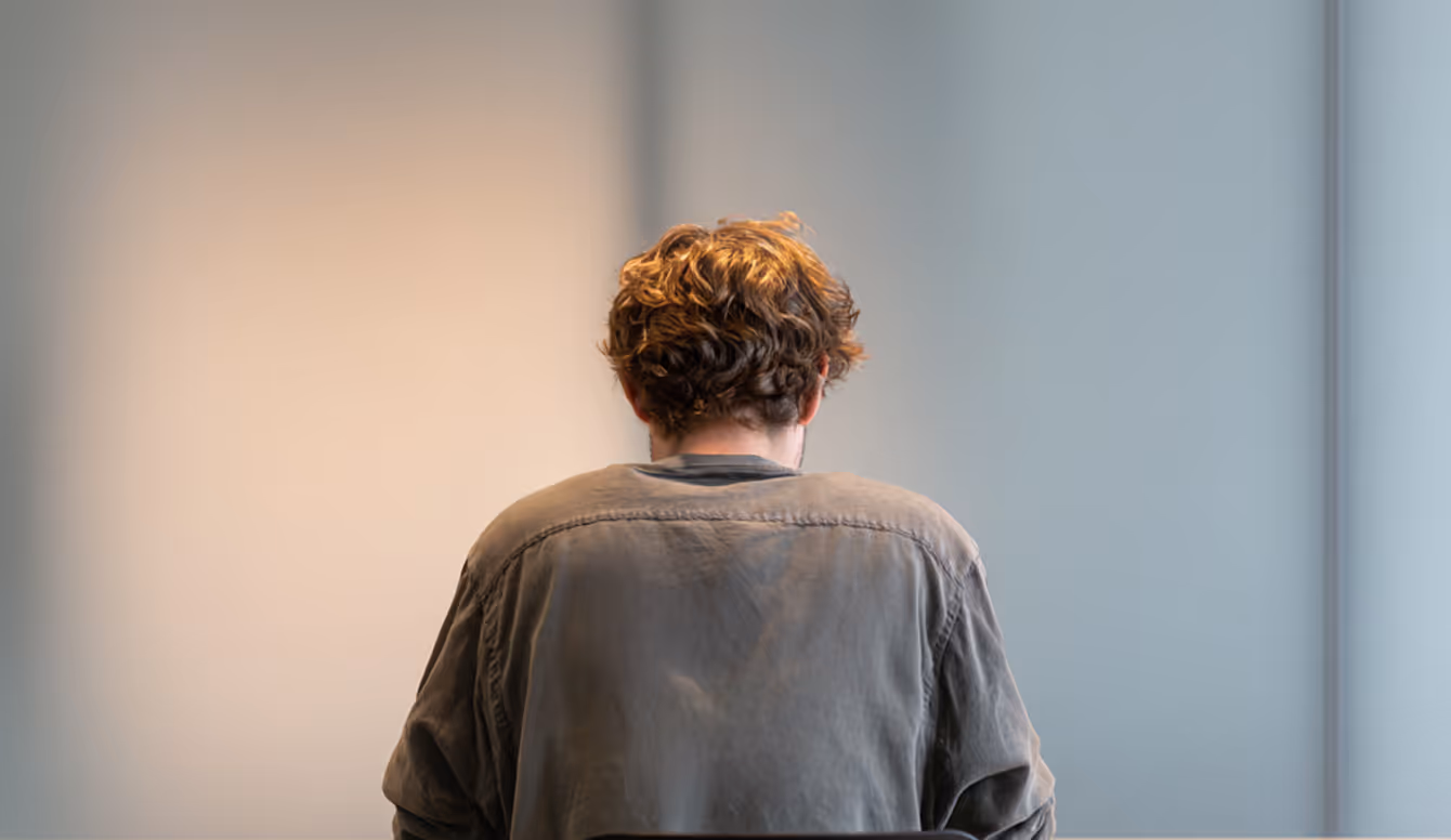 Man seated in a clinic room, viewed from behind